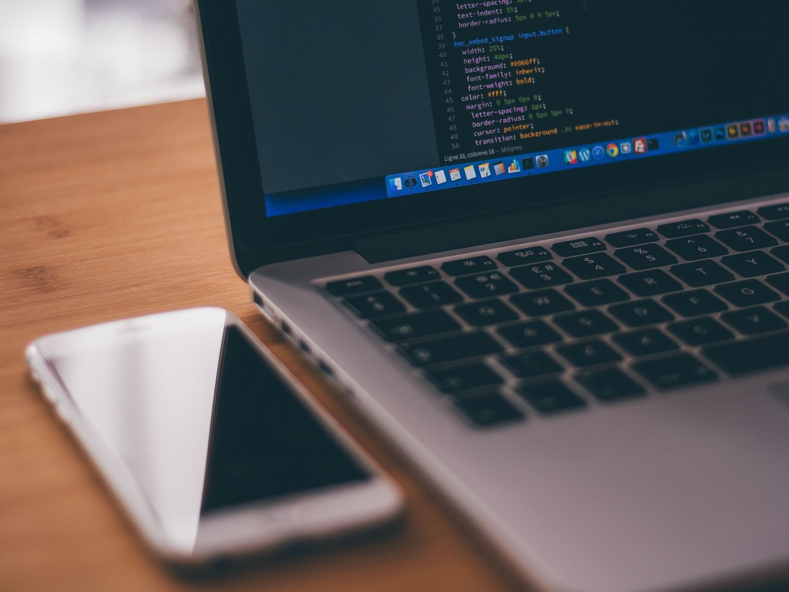Coding setup with laptop displaying code and smartphone on a wooden table, ideal for tech themes.