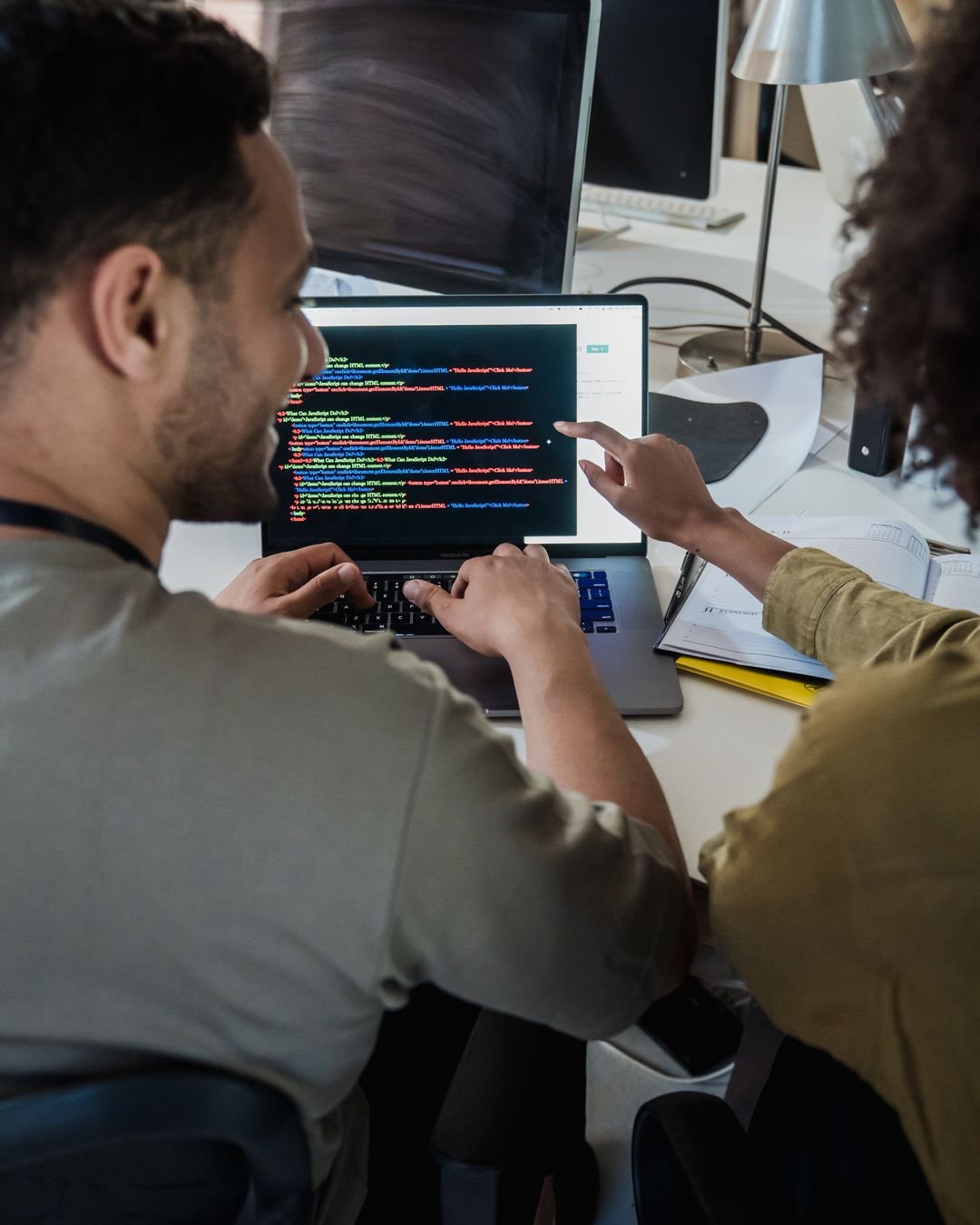 Two programmers working together on a laptop, discussing code in a modern office setting.