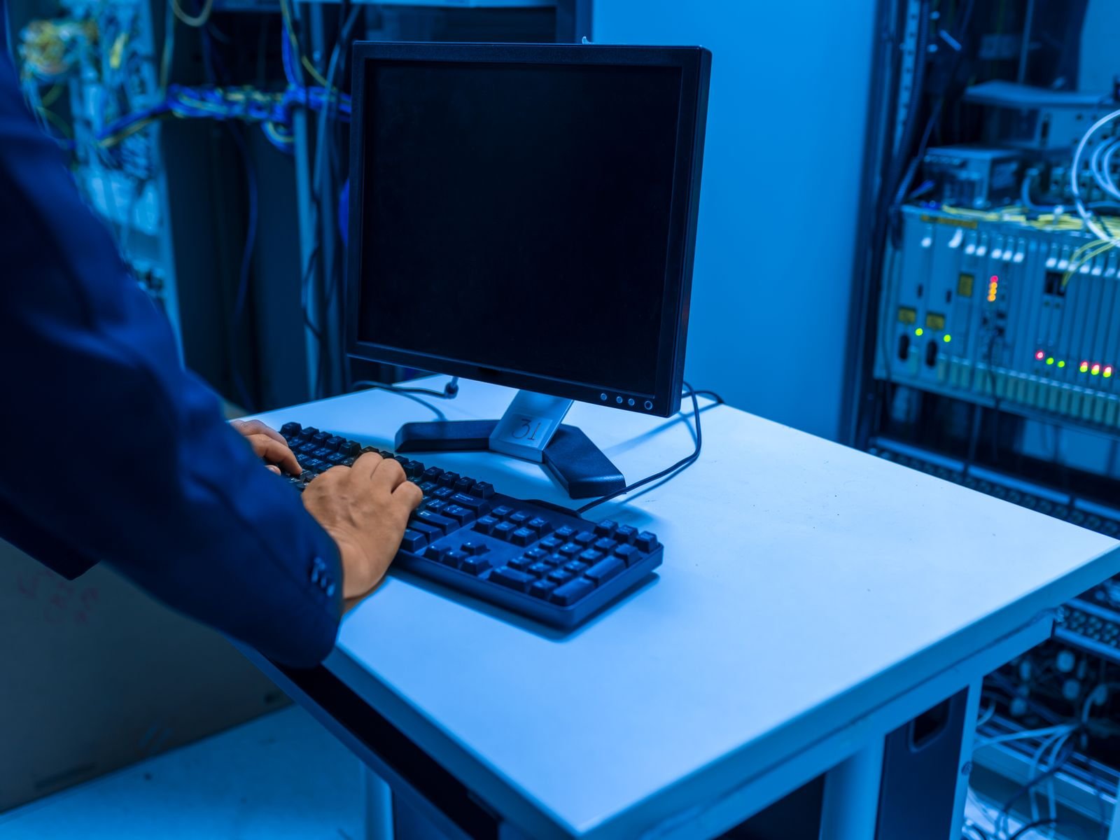 An IT professional operates a computer in a server room, managing network systems and connected devices.
